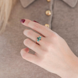 Rose gold marquise green moss agate engagement ring set with marquise opalescent sapphire and diamond accents paired with a chevron band displayed in hand against a warm brown background
