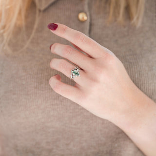 Sterling silver wedding band with leaf motif and marquise moss agate engagement ring displayed in hand against warm brown backdrop