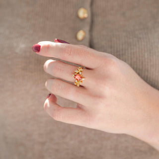 Yellow gold leaf engagement ring with oval-shaped fireworks-cut orange Padparadscha sapphire displayed in hand against warm brown backdrop