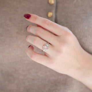 Silver marquise cut peachy pink morganite engagement ring with diamond accents displayed in hand against warm brown background