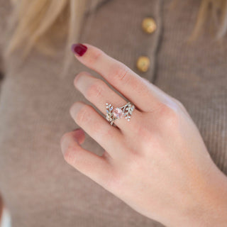 Silver leaf guard wedding band and oval fireworks-cut morganite engagement ring displayed in hand against warm brown backdrop
