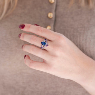 Silver crown tiara-inspired wedding band and pear-shaped blue sandstone engagement ring with amethyst accents displayed in hand against warm brown backdrop