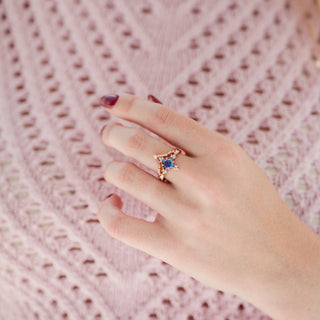 Rose gold princess/square-cut alexandrite engagement ring with diamond accent stones and wedding band displayed in hand against warm pink backdrop
