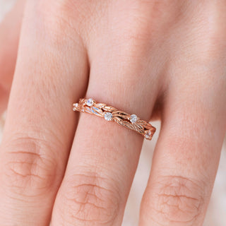 Rose gold wedding band with round diamond accents on hand over light background