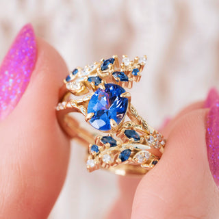 Hand holding gold ring with leaf design and blue sapphire center stone 