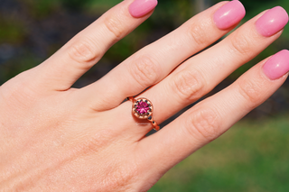 Vintage Ruby Ring in 14K Rose Gold Vermeil by Aquamarise, featuring a vibrant red ruby set in a delicate rose gold band, worn on a hand with pink nail polish against a natural green background.