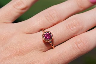 Vintage Ruby Ring in 14K Rose Gold Vermeil by Aquamarise, featuring a vibrant red ruby set in an elegant rose gold band worn on a hand against a blurred green background.