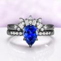 Art Deco Pear Blue Sapphire Ring Set in Black Ruthenium by Aquamarise, featuring a pear-shaped blue sapphire with sparkling white diamonds on polished black ruthenium bands.
