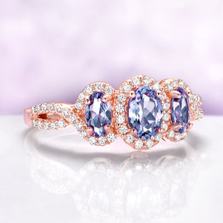 Rose gold ring with three purple gemstones on a light purple background