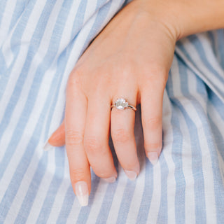 Three stone diamond ring on a hand against a blue and white background 