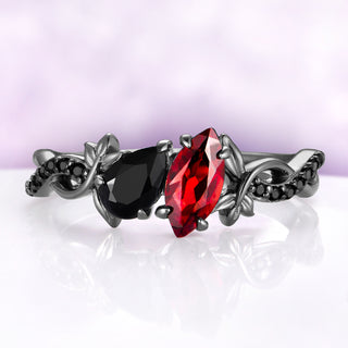 Toi Et Moi Garnet & Black Onyx Leaf Vine Engagement Ring in Black Ruthenium by Aquamarise, red marquise garnet beside a pear black onyx between blackened leaves
