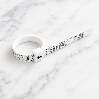 White plastic US ring sizer with numbered scale, shown on a marble surface