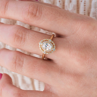 Yellow gold engagement ring with oval cut diamond center stone and diamond accents on hand over a light background 