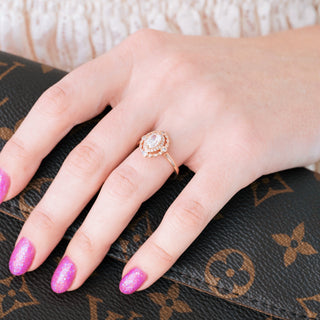 Rose gold engagement ring with oval cut diamond center stone and accents on hand over a dark background 