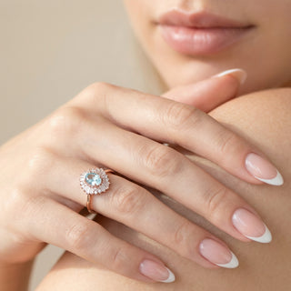 Close-up of a hand wearing a ring with a floral design on a neutral background