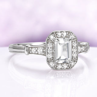 Diamond ring with emerald-cut center stone on a light purple background