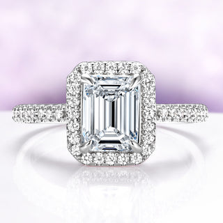Diamond ring with emerald-cut center stone and halo on a light purple background