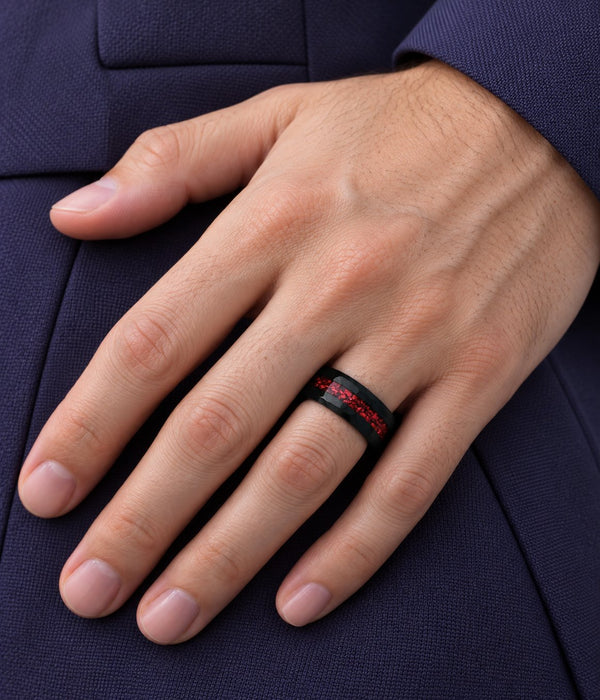 Man's hand resting on a navy suit wearing a black wedding band with crushed red inlay, Aquamarise banner