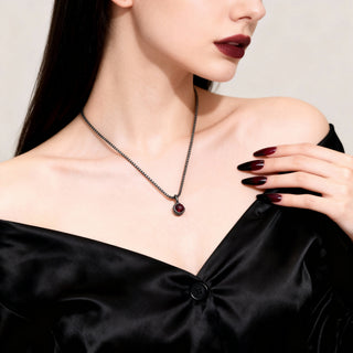 Woman wearing a black necklace with a red gemstone against a neutral background