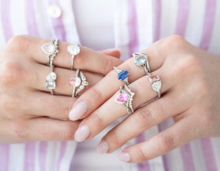 Aquamarise Two hands wearing multiple rings with various gemstones against a striped background