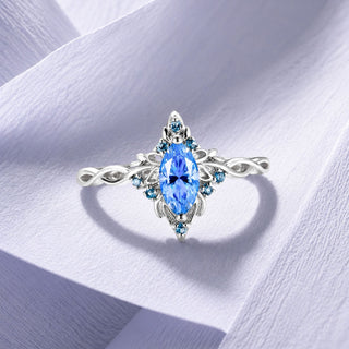 Sterling silver marquise blue gemstone ring with an infinity twist band and blue pave accents on lilac paper, Aquamarise collection banner
