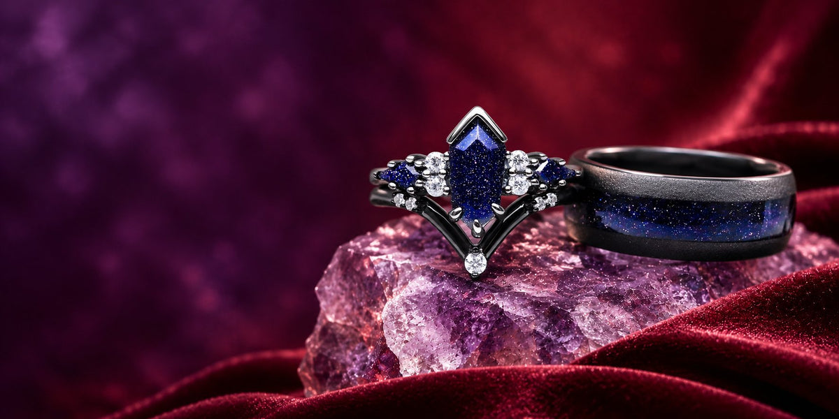 Couples ring set on an amethyst cluster over red velvet: black kite-cut blue sandstone engagement ring with chevron band beside a black men's band with blue sandstone inlay, Aquamarise banner
