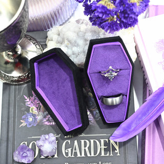 Angled view of the black coffin ring box and lid showing the depth of the purple velvet interior