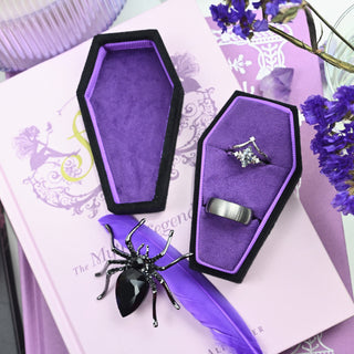 Open black and purple coffin ring box showing the two ring slots and the purple-lined lid