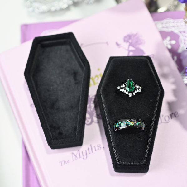 Black velvet coffin ring box holding an engagement ring and a wedding band, with the lid beside it