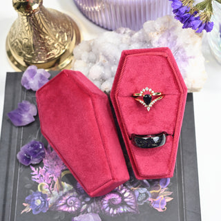 Red velvet coffin ring box with its lift-off lid resting alongside, two rings inside