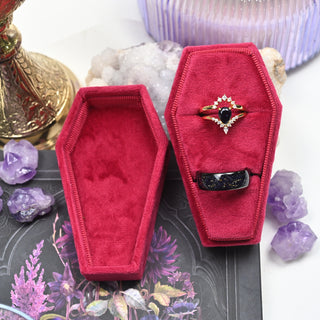Open red coffin ring box showing the two ring slots and the velvet-lined lid, styled with amethyst crystals