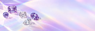 Loose lilac and lavender gemstones in round, emerald, cushion, oval and pear cuts on a pale lilac surface with rainbow prism light, Aquamarise Compassion page banner