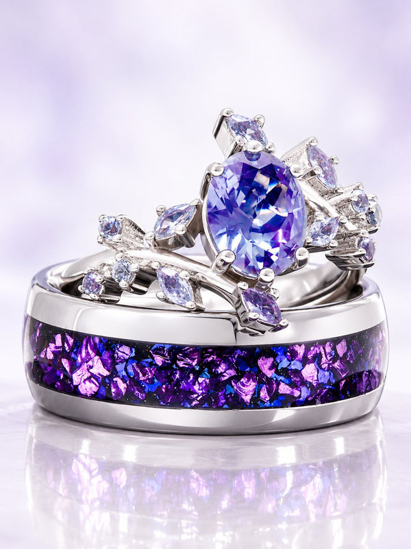 Couples ring set on lilac satin: oval blue-violet gemstone leaf ring with marquise accents resting on a silver men's band with crushed purple inlay, Aquamarise banner