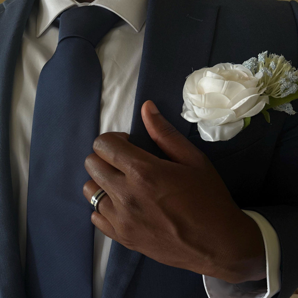 Groom in a navy suit with a white boutonniere wearing a crushed blue sapphire men's wedding band in silver tungsten carbide – Aquamarise customer photo