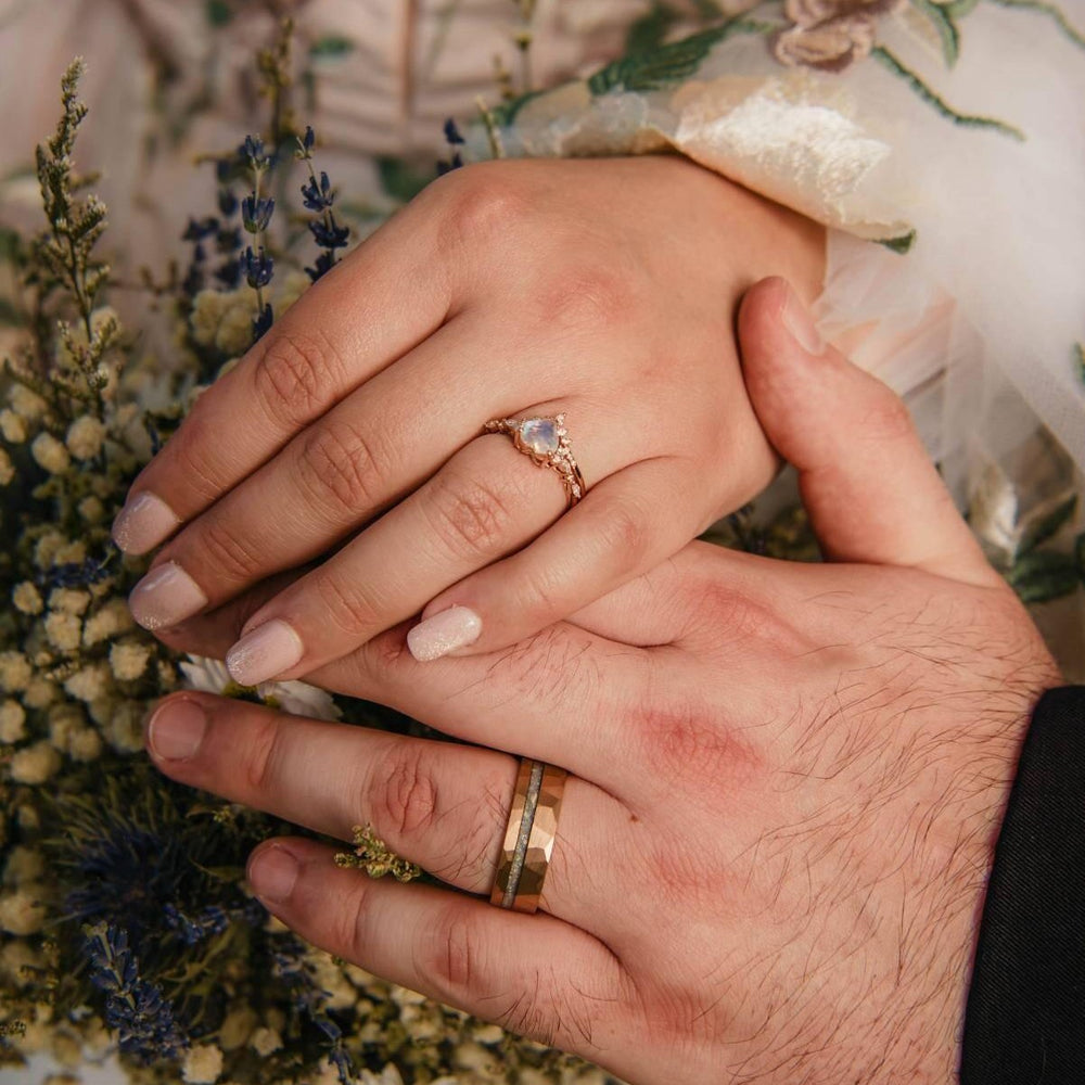 Couple's hands resting on a dried-flower bouquet, the groom wearing a crushed moonstone hammered men's wedding band in rose gold tungsten – Aquamarise customer photo