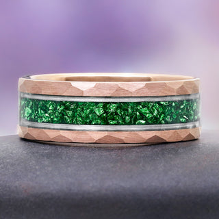 Ring with green gemstone inlay on a gray surface with a purple gradient background