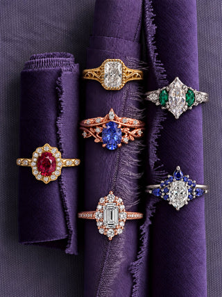 Six engagement rings on rolls of purple fabric: radiant moissanite filigree ring, Estée sapphire and diamond set, Cordelia oval ruby, fantasy-cut purple sapphire leaf set, Emerie emerald and diamond set and emerald-cut diamond in rose gold, Aquamarise banner