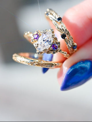 Gold ring with a large diamond held by a hand with blue nail polish.