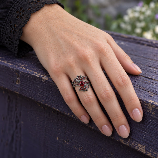 Natural Garnet Trillion Bat Ring Set in black ruthenium worn on the hand, resting on a purple stone wall