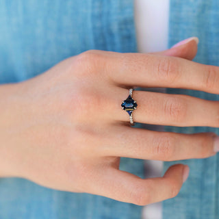 Hand wearing a ring with a blue gemstone against a blue denim background