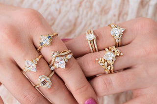 Multiple gold rings with diamond gemstones on a hand against a neutral background