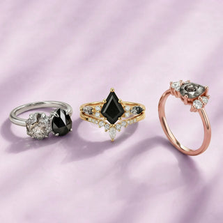 Three rings with black and white gemstones on a pink background