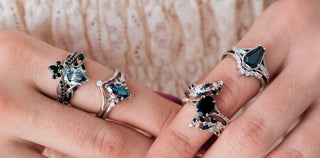 Two hands wearing silver rings with black gemstones on a neutral background