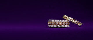 Stacked diamond eternity bands and a gold leaf ring on purple velvet
