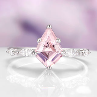 Ring with a pink diamond and smaller clear diamonds on a reflective surface with a blurred purple background