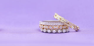 Stacked pave eternity bands in silver, rose gold and yellow gold beside a yellow gold leaf band on a lilac background, Aquamarise Labor Day sale banner
