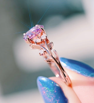 Rose gold ring with a large pink gemstone held by a hand with blue nail polish.