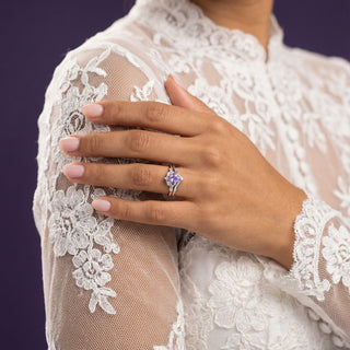 Hand wearing a ring with a purple gemstone on a lace garment against a dark background