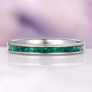 Silver ring with a green gemstone inlay on a reflective surface with a purple gradient background