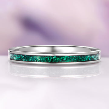 Silver ring with a green gemstone inlay on a reflective surface with a purple gradient background